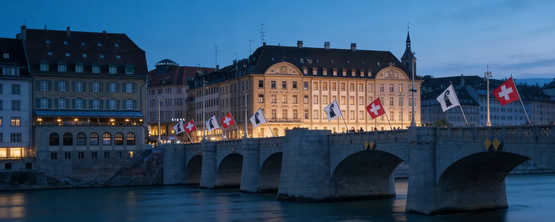 Beleuchtete Brücke mit Schweiz-Flaggen in Basel bei Abenddämmerung, stimmungsvolle Stadtansicht am Rhein.
