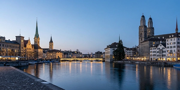 Abendstimmung in Zürich mit Blick auf die beleuchtete Altstadt und den Fluss Limmat.