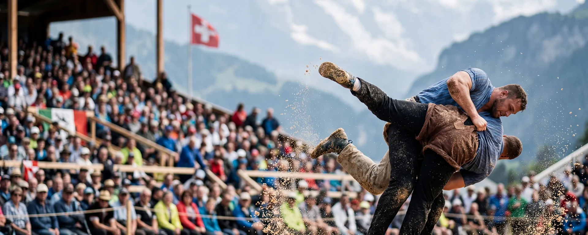 Schweizer Schwingen-Wettkampf mit zwei Ringern in Aktion, vor einer großen Zuschauermenge und den Alpen im Hintergrund.