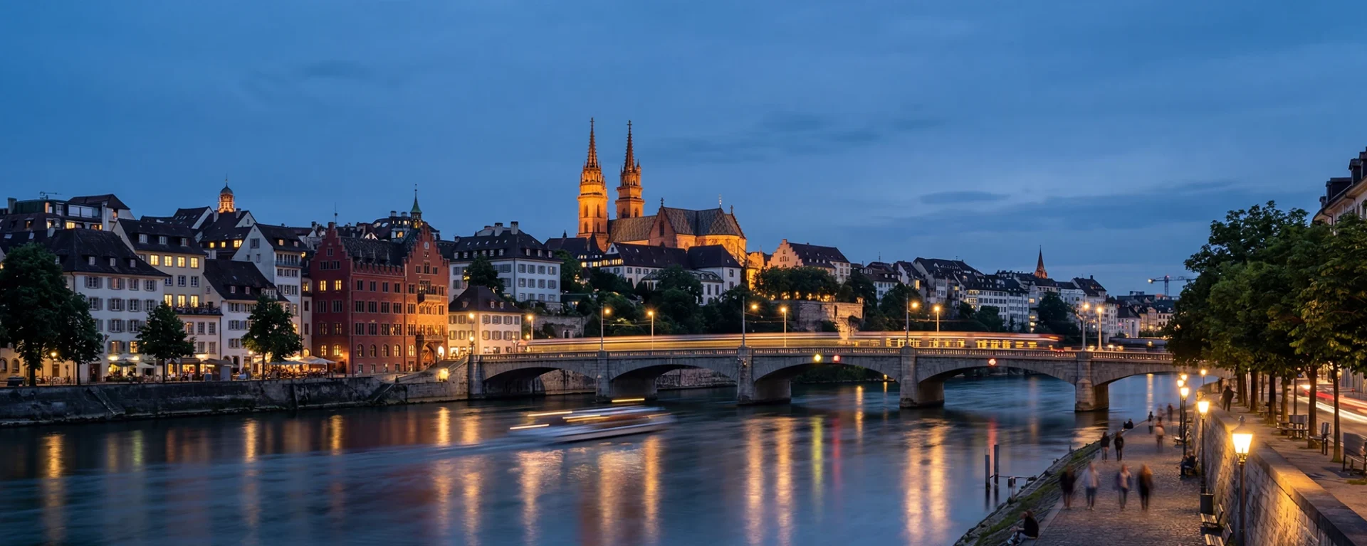 Basel bei Abenddämmerung: Beleuchtete Mittlere Brücke und Altstadt mit Münster, spiegelnd im Rheingewässer.